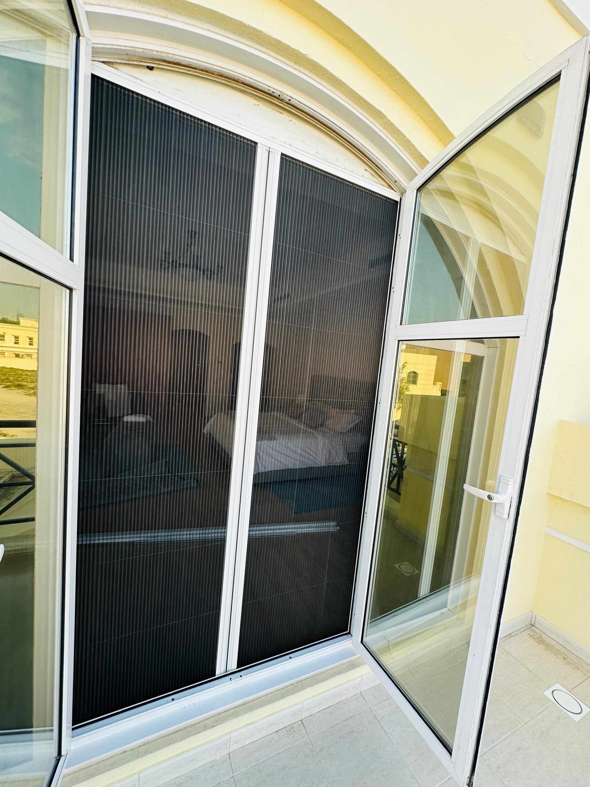 Both halves of a double fly screen rolled away beside a glass wall in Dubai
